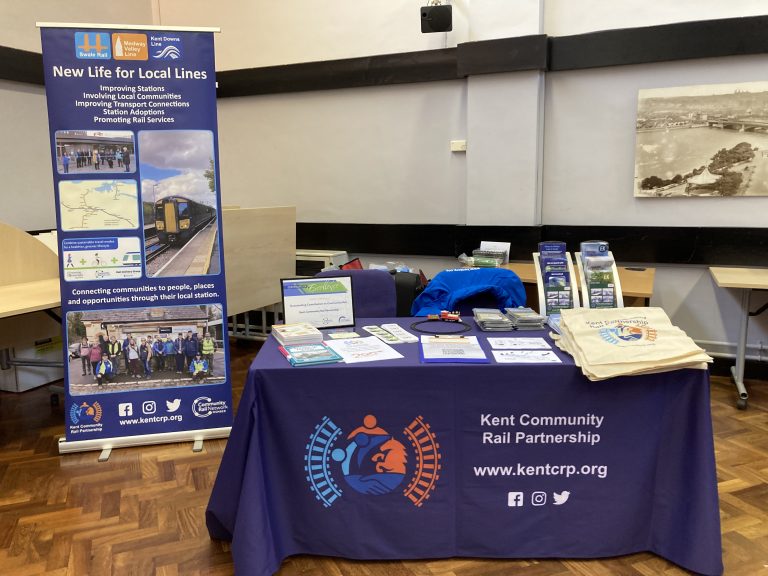 Kent Community Rail partnership promotional stall with a variety of merchandise and leaflets, beside a roller banner promoting the rail partnership