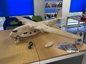 A sculpted model of a wooden sea plane on a desk. The model is undergoing restoration and is only partially complete