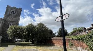 Signs for Strood Community trail attached ot a lamppost beside a path through a churchyard.