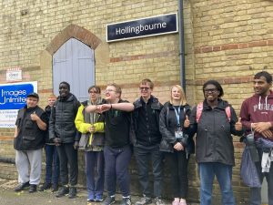 A group of people pose for a picture under a sign for Hollingbourne station