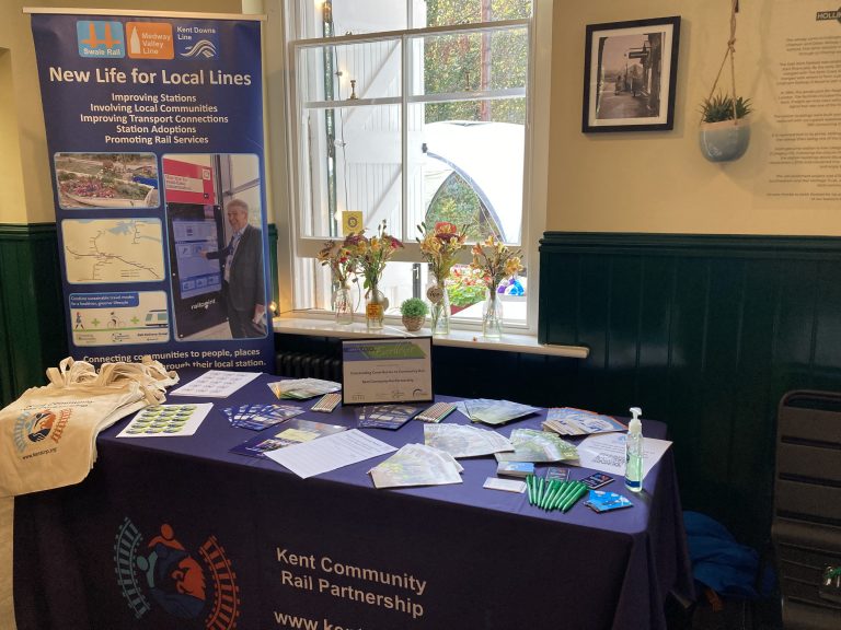 The Kent Community Rail Partnership promotional roller banner and table of giveaway items including tote bags, stickers and brochures.