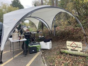 A pop up shelter above tables of cooking equipment. A sign to one side reads "The station at Hollingbourne"