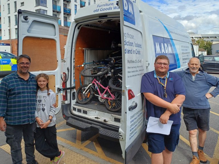 Four people pose for a picture beside a van from Make a Difference to Maidstone. The van doors are open, it is loaded with bikes