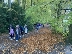 A group of people walk towards camera on a wide road, the surface is covered with Autumn leaf fall.