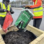 Two people in hi-vis empty bags of soil and compost into a wooden planter