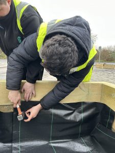 A person in hi-vis secures a plastic liner into a wooden planter
