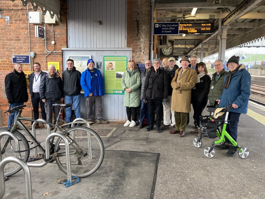 A crowd of people gathered on the platform at Paddock Wood station, pose for a photo beside the new Colonel Stephens information panel.