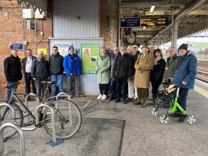 A crowd of people gathered on the platform at Paddock Wood station, pose for a photo beside the new Colonel Stephens information panel.