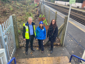 Three people pose for a photo at the entrance gate to the nature garden at Charing station