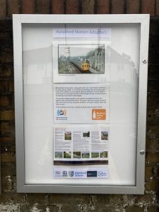 A closed poster cabinet headed "Aylesford Station Adopters" displays a colour image of a slam-door train the station and details of its history. A poster gives information about places to visit on the Medway Valley Line, Logos of Kent Community Rail Partnership, Aylesford Parish Council, Aylesford Schoo;, Southeastern and Community Rail Network Funded.