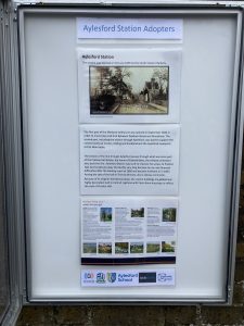 An open poster cabinet headed "Aylesford Station Adopters" displays a sepia image of the station and details of its history. A poster gives information about places to visit on the Medway Valley Line, Logos of Kent Community Rail Partnership, Aylesford Parish Council, Aylesford Schoo;, Southeastern and Community Rail Network Funded.