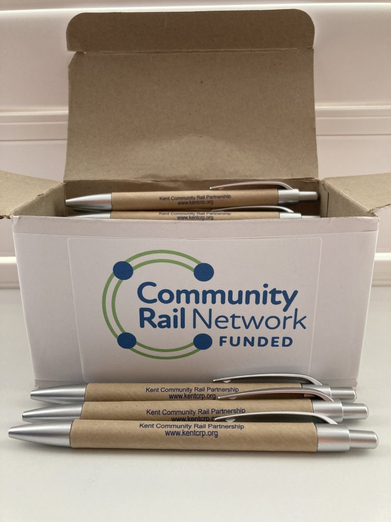 A box full of pens. The box is labelled Community Rail Network Funded. In front of the box are three pens with the wording Kent Community Rail Partnership, kentcrp.org