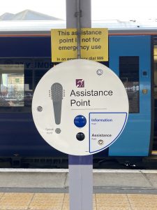 A circular assistance point on a train platform. There are buttons for Information and Assistance. A notice above explains the assistance point is not for emergency use.