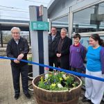 Chris cuts a ribbon above a planter on the platform of a station while people look on