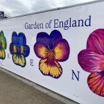 A vinyl on the side of a byilding featuring flowers and "Garden of England" at the top and "KENT" in individual letters between the flowers.