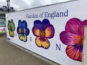 A vinyl on the side of a byilding featuring flowers and "Garden of England" at the top and "KENT" in individual letters between the flowers.
