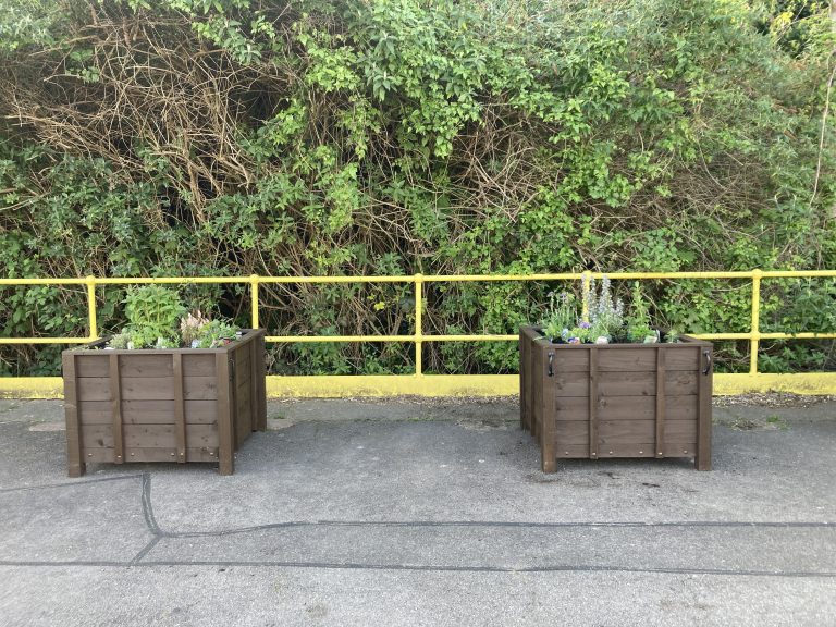 A pair of wooden planters with fresh planting on a station platform.