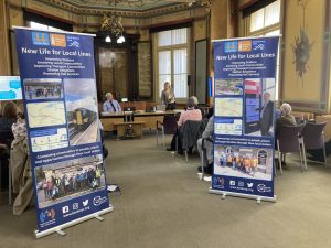 Two roller banners promoting Kent Community Rail Partnership in Maidstone Town Hall. Beyond them people are seated listening to a presentation