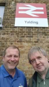 Selfie of Gary and Michael standing beneath the Double Arrow logo sign at Yalding station.