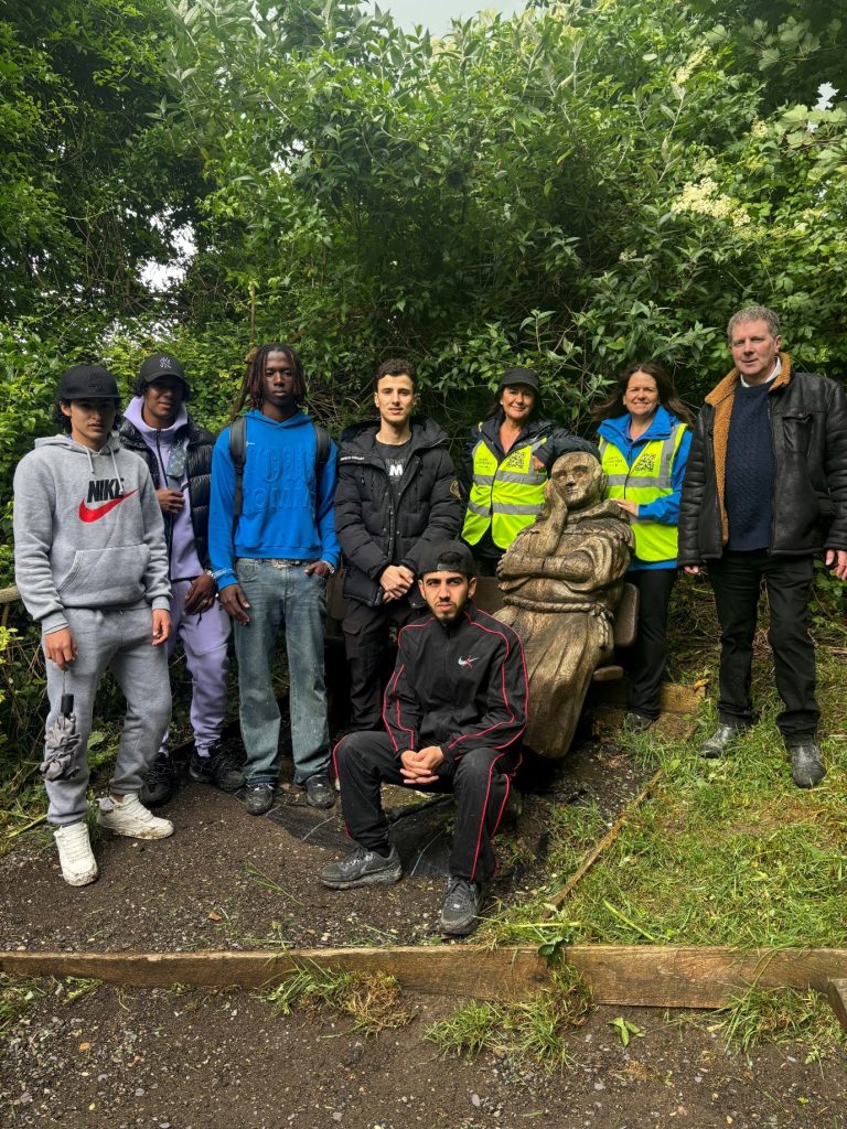 Students and walk leaders pose for a picture alongside the carved wooden statue of Percy the Pilgrim.