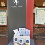 A box of treat bags from the Lenham school containing positive messages and a variety of chewy sweets. The box is on a table in front of a roller banner with the school's white horse logo.