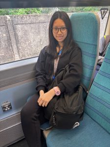 A person wearing a black jacket and trousers with a black bag beside them sitting onboard a train.