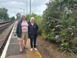 Two people standing on a station platform beside a planted garden bed