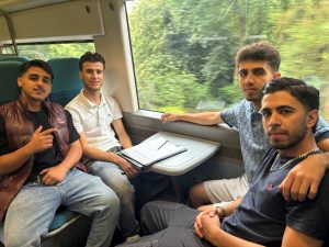 Four people sat around a table onboard a train. They are all casually dressed.
