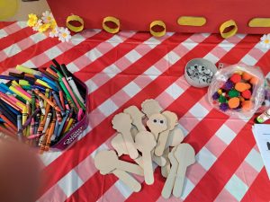 On a table top are colouring materials, googly eyes, felt bobbles and cut out faces on sticks