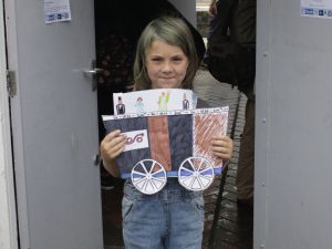 A child stands in a doorway and holds up a drawing of a railway wagon and some passengers