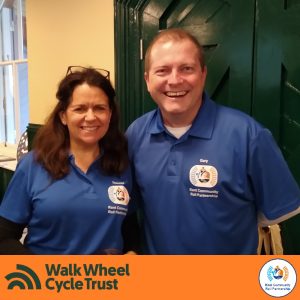 Therese and Garysmiling as they pose for a picture. They are wearing blue Kent Community Rail Partnership polo shirts. An orange footer displays the logos of Walk Wheel Cycle Trust and Kent Community Rail Partnership.