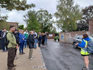 Therese talks to a group of people admiring painted murals on a wall. The murals depict nuns and monks riding bicycles past a signpost.