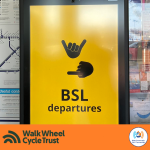 A large display screen with hand shapes "BSL departures". An orange footer displays the logos of Walk Wheel Cycle Trust and Kent Community Rail Partnership.