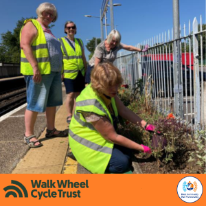 Four people, three in hi-vis jackets, on a narrow station platform. They are tending to flowers planted in beds. An orange footer displays the logos of Walk Wheel Cycle Trust and Kent Community Rail Partnership.
