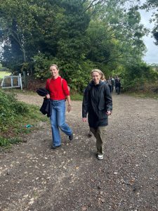 A group of people walk along a gravel path in woodland. The sky above is grey.