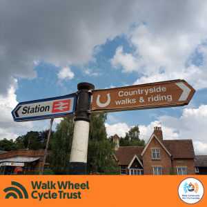 A fingerpost indicating directions to a Station and Countryside Walks and Riding. An orange footer displays the logos of Walk Wheel Cycle Trust and Kent Community Rail Partnership.