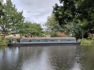 A green houseboat moored beneath trees on the far bank of a river