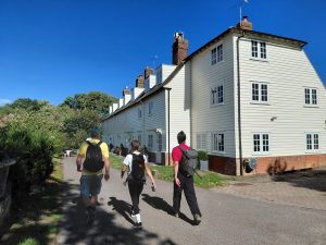 James, Roxy and Mike walk past a row of white weatherboarded cottages.