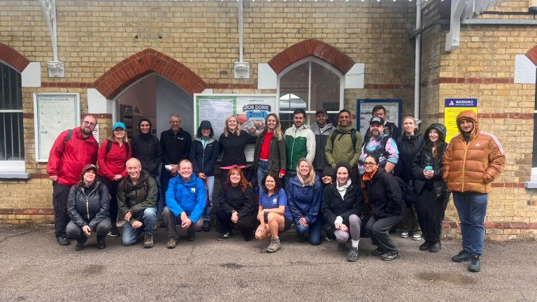 A group of over 20 people pose for a picture outside a station