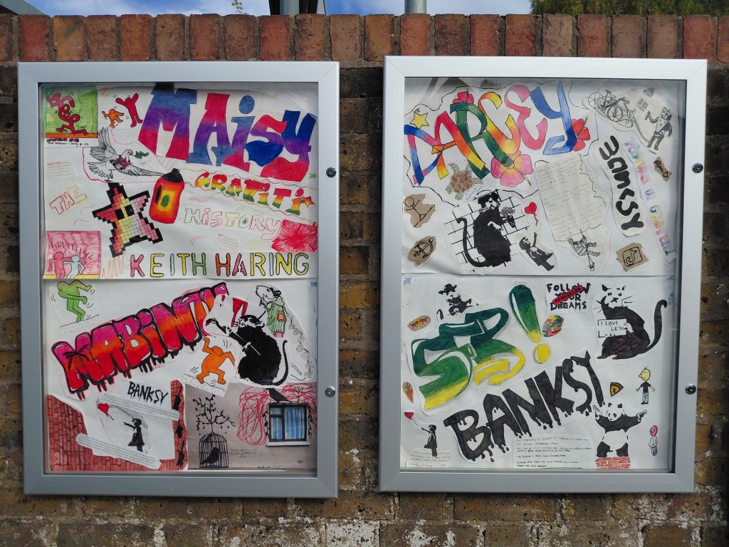 A pair of display cabinets mounted on a wall. The cabinets contain a variety of graffiti styled artwork and some notes on the history of the genre.