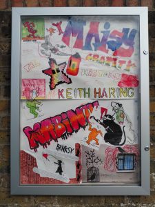 A display cabinet mounted on a wall. The cabinet contains a variety of graffiti styled artwork.