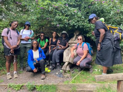 A group of people, most with back-packs, gathered around a wooden carving of a monk, pose for a photo